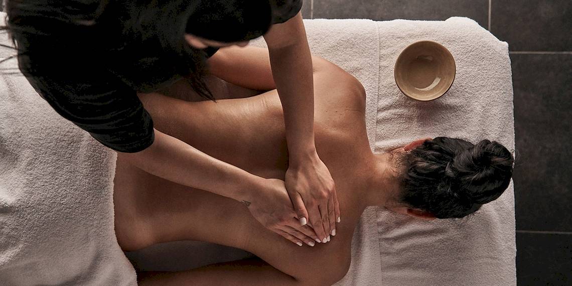 Massagebehandlung im Myconian Avaton Resort mit einer Frau, die einen Rückenmassiert.