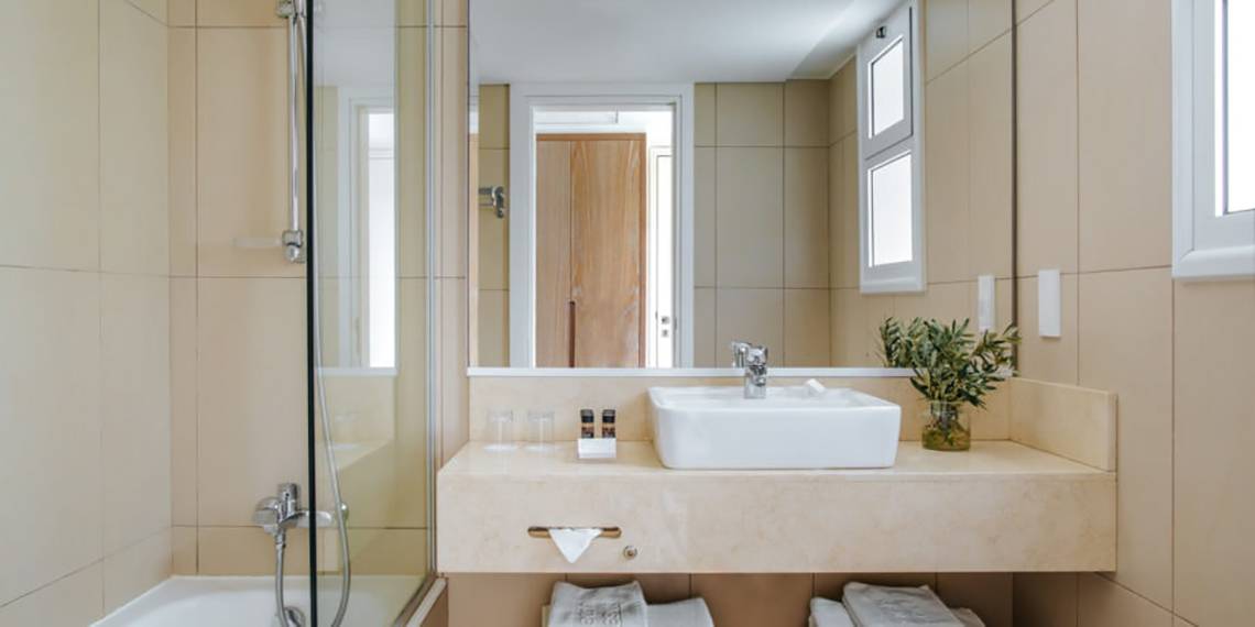 Badezimmer im Nissi Beach Resort mit einer Dusche, einem Waschbecken und einem Spiegel.
