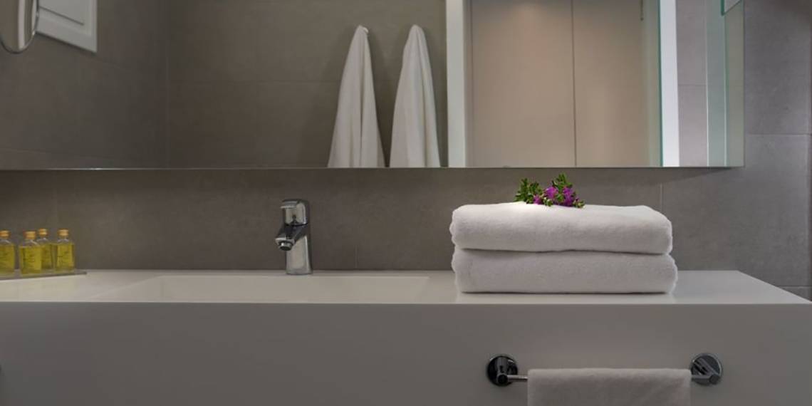 Ein Badezimmer im Nissi Beach Resort mit einem Waschbecken, Spiegel und gestapelten Handtüchern.