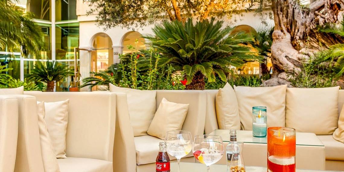VIVA Golf Adults Only Hotel Lounge mit weißen Sofas, Kissen, und Pflanzen im Hintergrund.