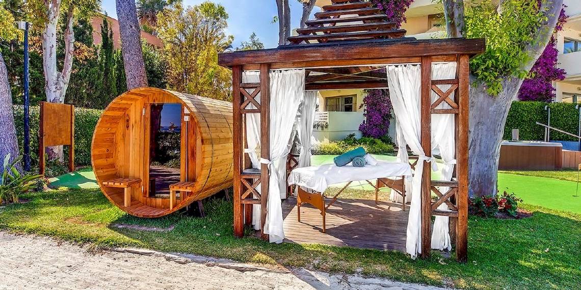 Außenbereich des Viva Golf Adults Only Hotels mit einer Holzsauna und einem Massagetisch unter einer Pergola.