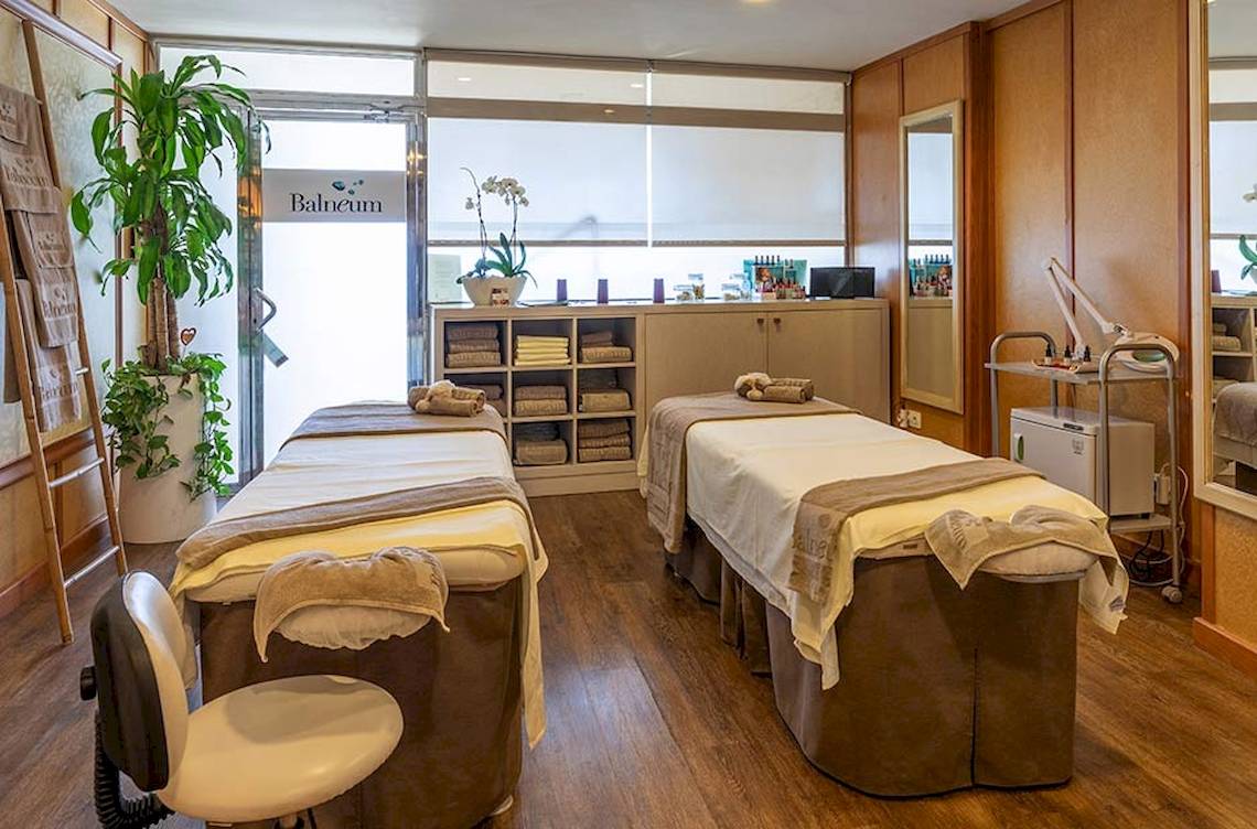Behandlungsraum im Balneum mit zwei Massagetischen, holzigen Möbeln und Pflanzen.