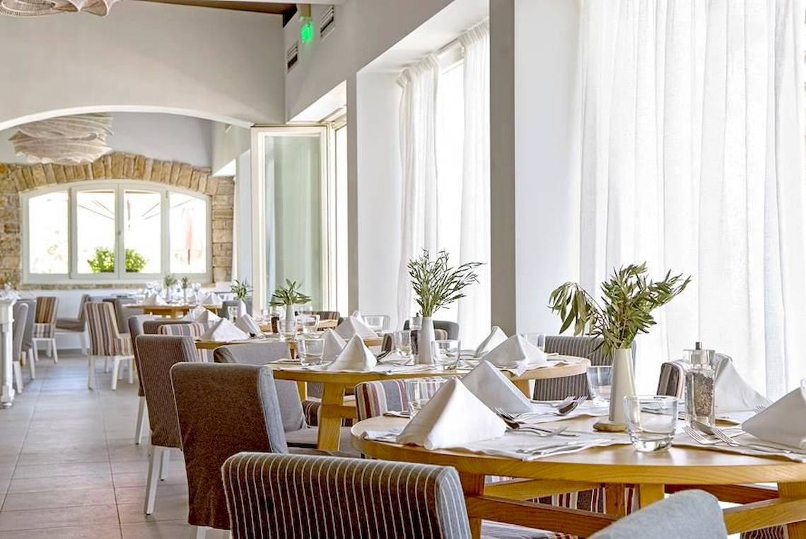 Innenbereich des Doryssa Seaside Resort Restaurants mit gedeckten Tischen und grünen Pflanzen in Vasen.