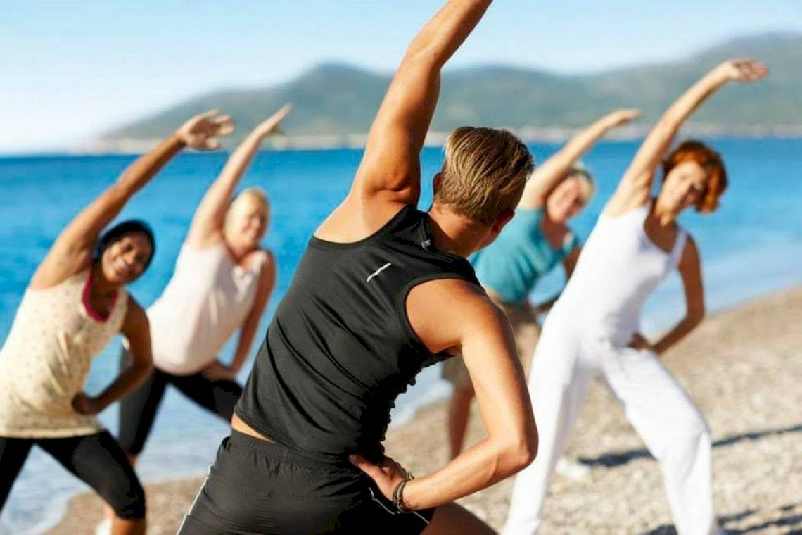 Gruppe von Frauen und Männern, die Yoga am Strand des Doryssa Seaside Resort machen