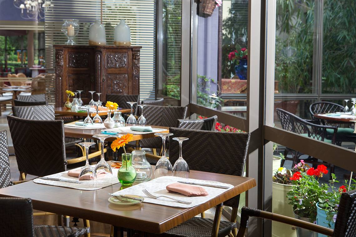 Innenansicht des Dionysos Hotel Restaurants mit gedeckten Tischen, Blumen und Ausblick auf den Garten.
