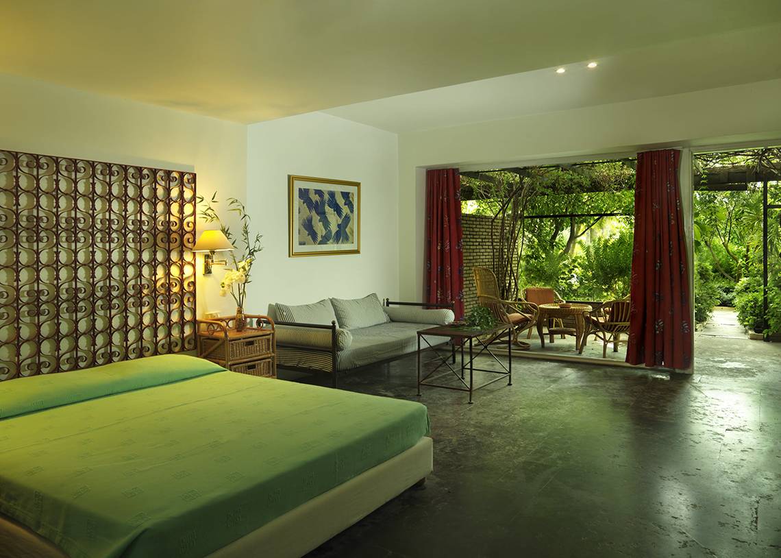 Innenansicht eines Zimmers im Dionysos Hotel mit einem Bett, einer Couch und einem Tisch mit Gartenblick.