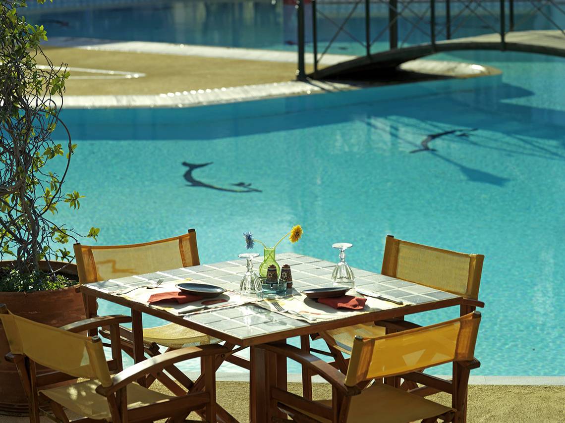 Gartentisch am Pool des Dionysos Hotels mit Blick auf das Wasser.