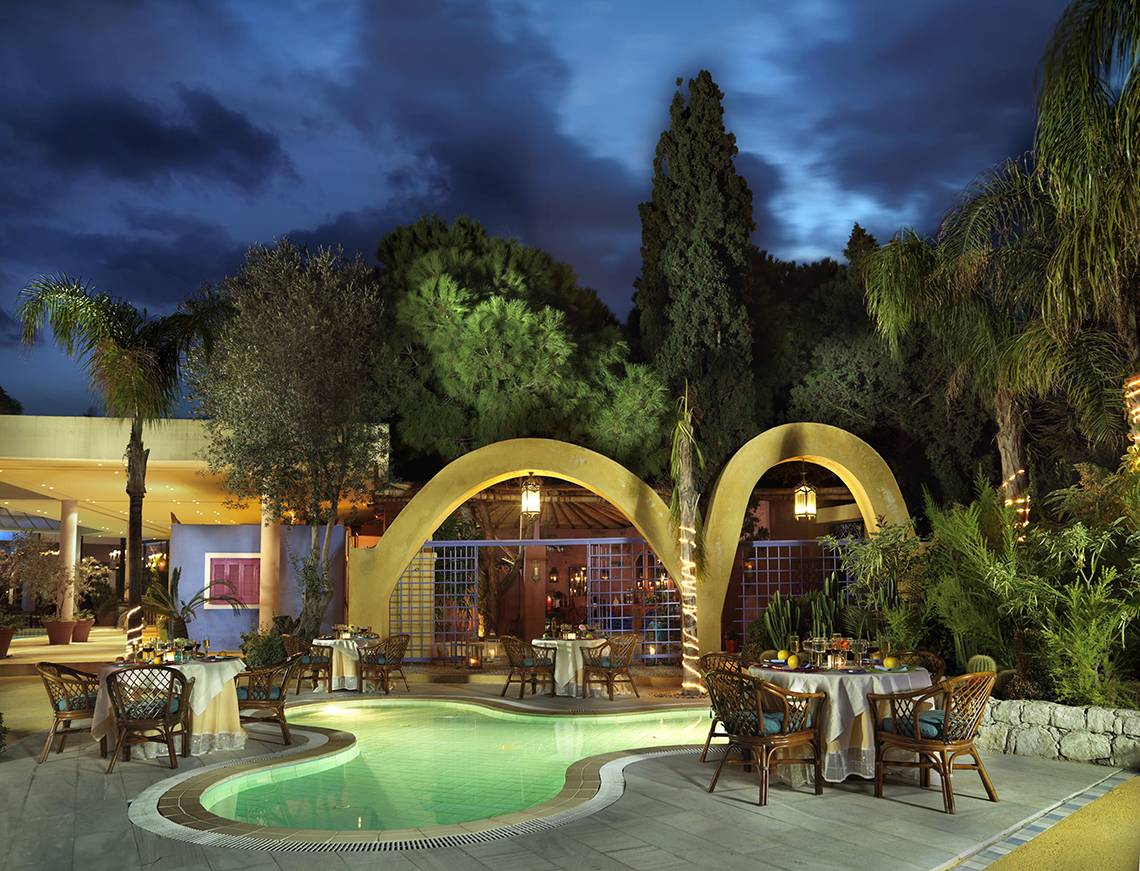 Außenbereich des Dionysos Hotels bei Nacht mit beleuchtetem Swimmingpool und runden Arkaden.