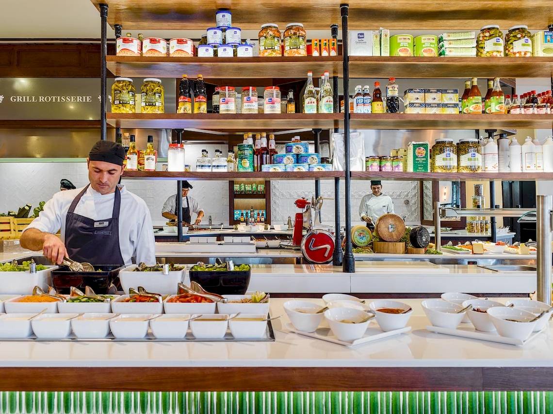 Koch im H10 Rubicon Palace bereitet Gerichte in der Grill Rotisserie zu, mit Zutaten und Utensilien um ihn herum.