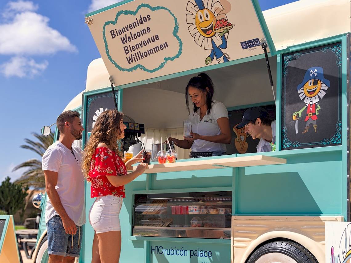 Zwei Gäste stehen an der Eiswagen-Theke von H10 Rubicon Palace, eine Frau serviert ihnen Getränke.