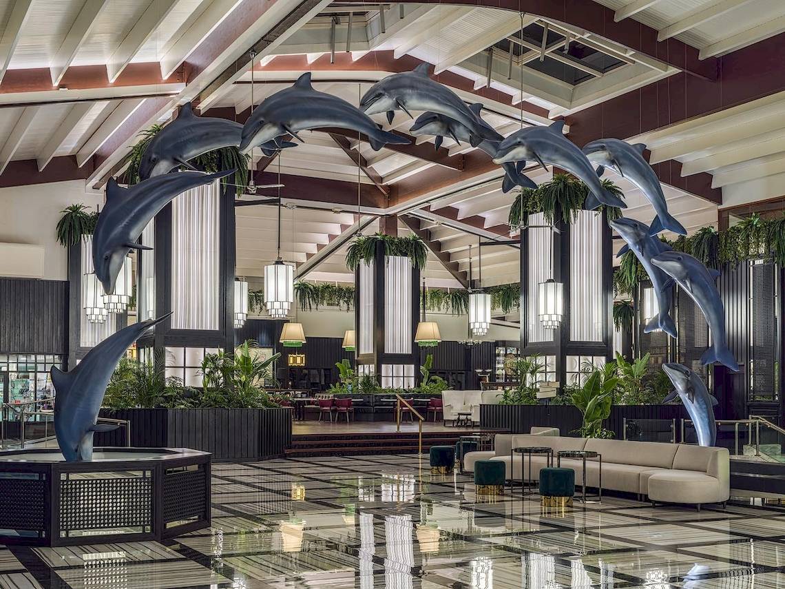 Ein Bild von der Lobby des H10 Rubicon Palace Hotels mit Delfin-Skulpturen, Pflanzen und Möbeln.