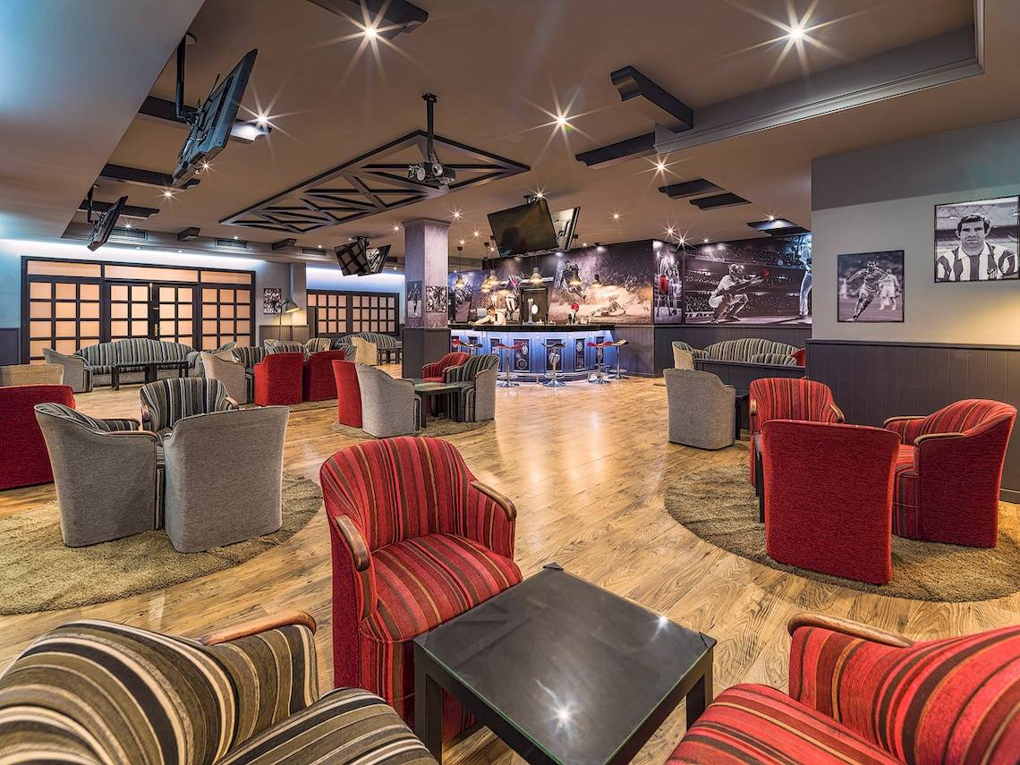 Lobby-Lounge-Bereich des H10 Rubicon Palace Hotels mit rot und grau gestreiften Sesseln und Tischen auf hölzerne Boden.