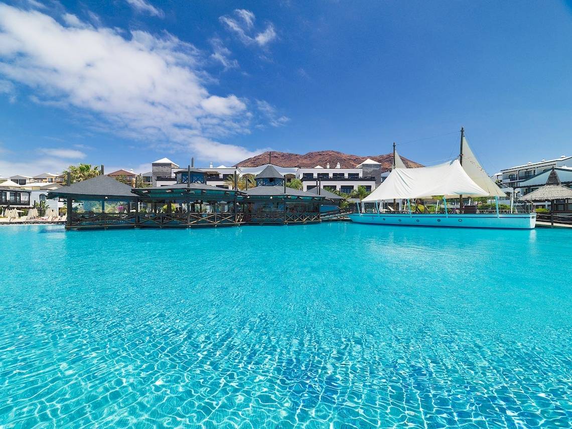 Das H10 Rubicon Palace Hotel mit einer blauen Poollandschaft im Hintergrund.