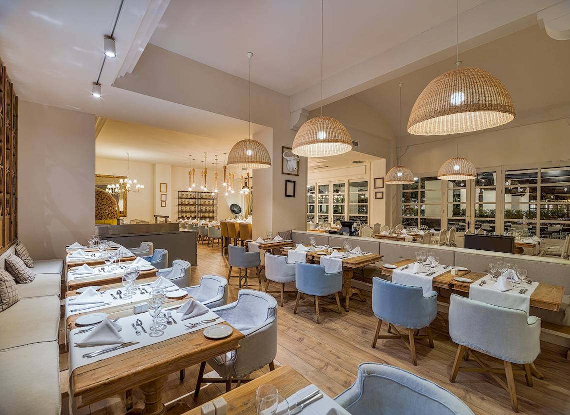 Innenraum des H10 Rubicon Palace Restaurants mit blauen Stühlen und Holztischen.