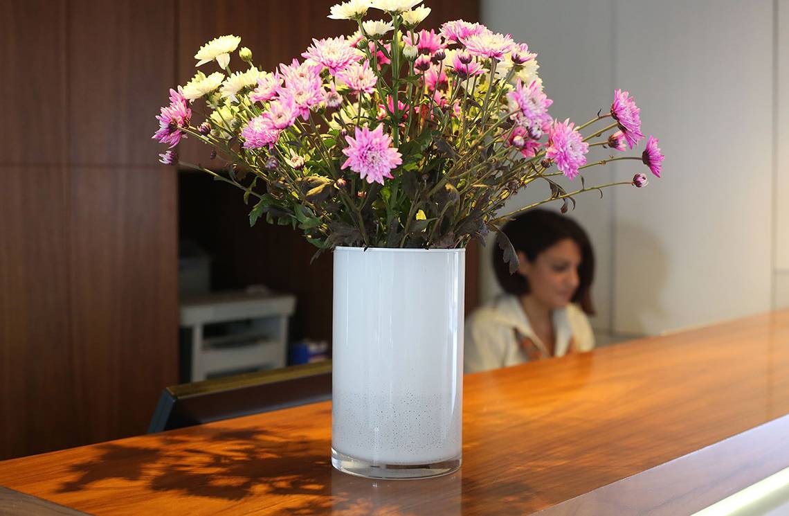 Eine weiße Vase mit bunten Blumen steht auf einem hölzernen Tisch.