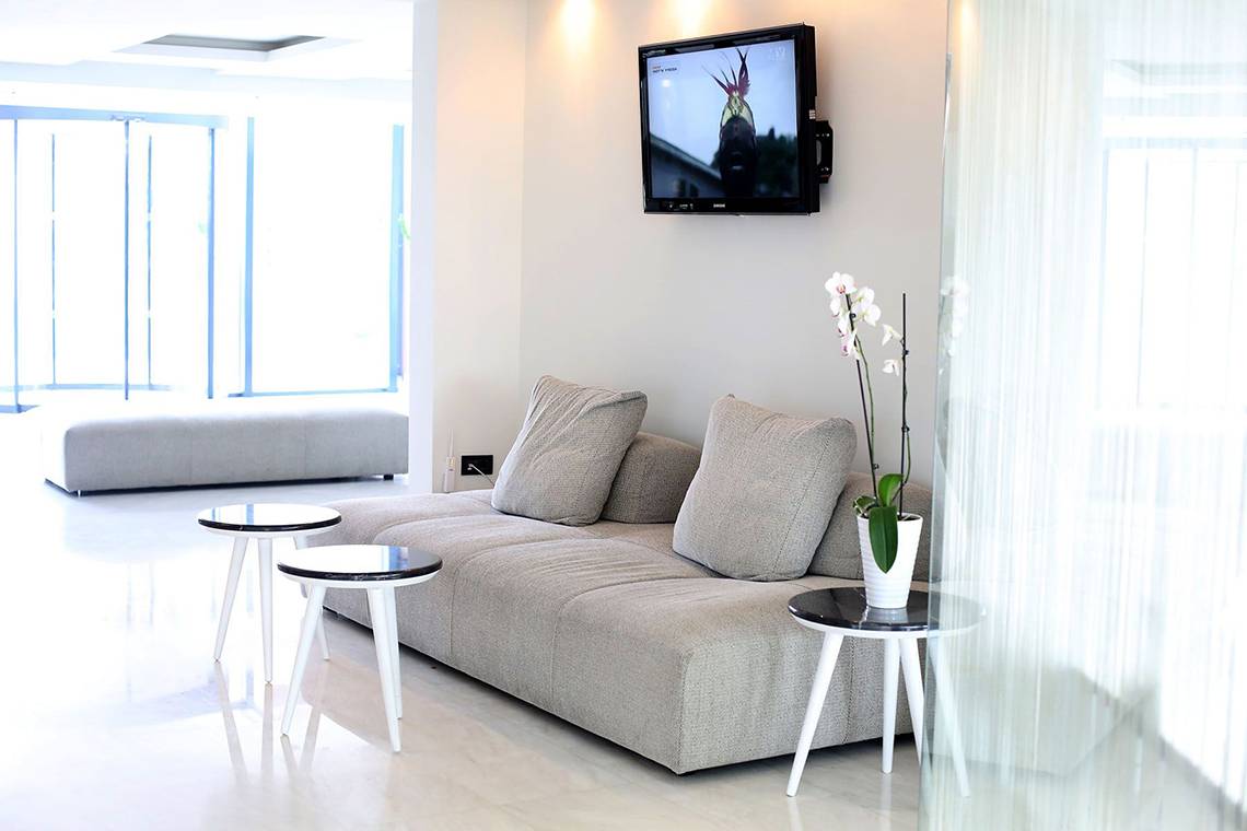 Wohnbereich im Minos Mare Royal Hotel mit grauer Couch, Beistelltischen und Fernseher.