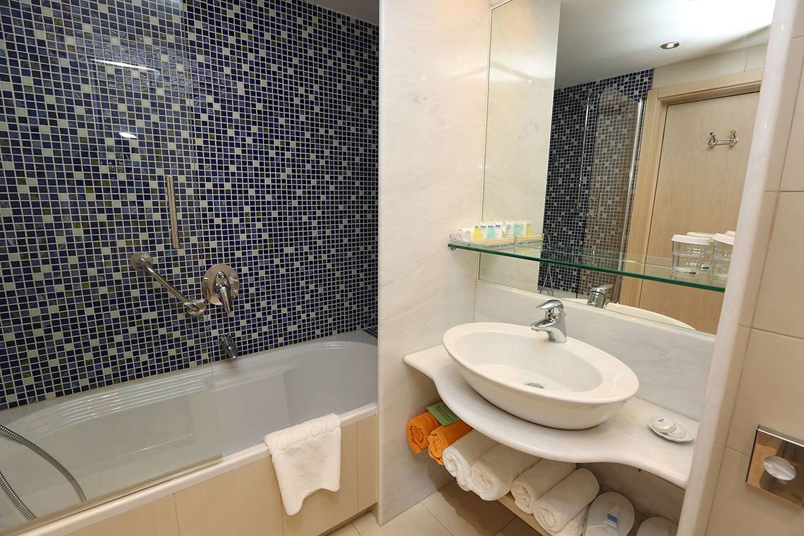 Badezimmer im Minos Mare Royal Hotel mit Badewanne, Waschbecken und blauen Fliesen.
