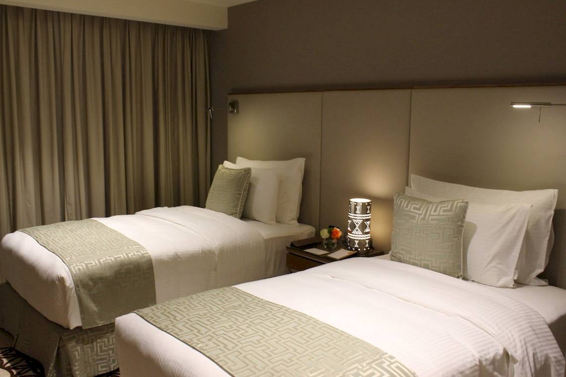 Zwei Betten mit cremefarbenen Bezügen und weißen Kissen im Hotelzimmer des Grand Millennium Muscat.