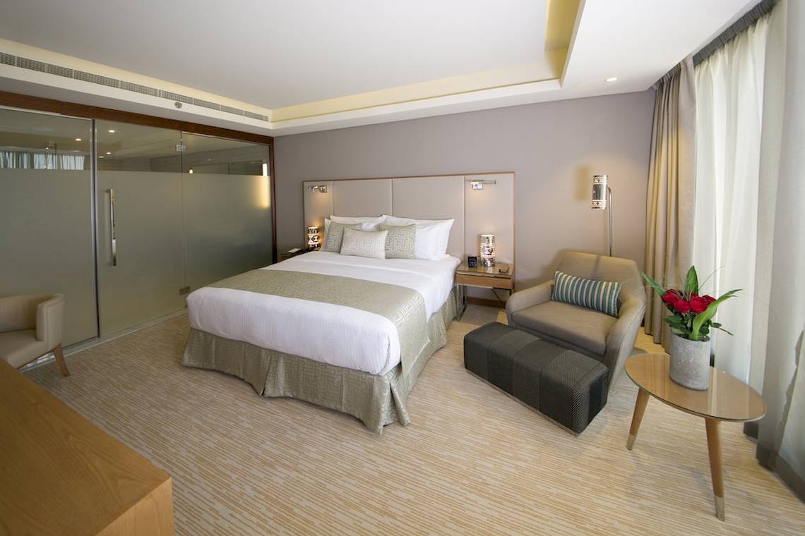 Hotelzimmer im Grand Millennium Muscat mit Doppelbett, Sesseln und Tisch mit Blumen.