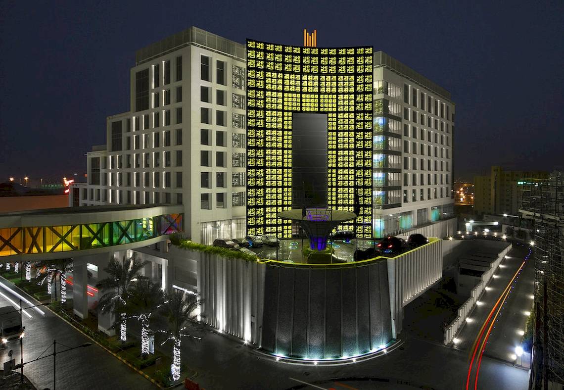 Grand Millennium Muscat Hotel aus der Luft bei Nacht, hell beleuchtet, mit Wasserfall und Brücke