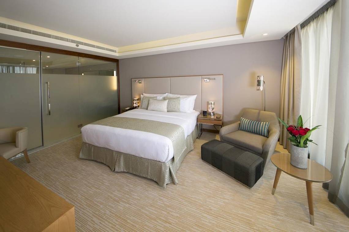 Doppelbettzimmer im Grand Millennium Muscat Hotel mit bequemen Sesseln, Tisch und Blumenvase.