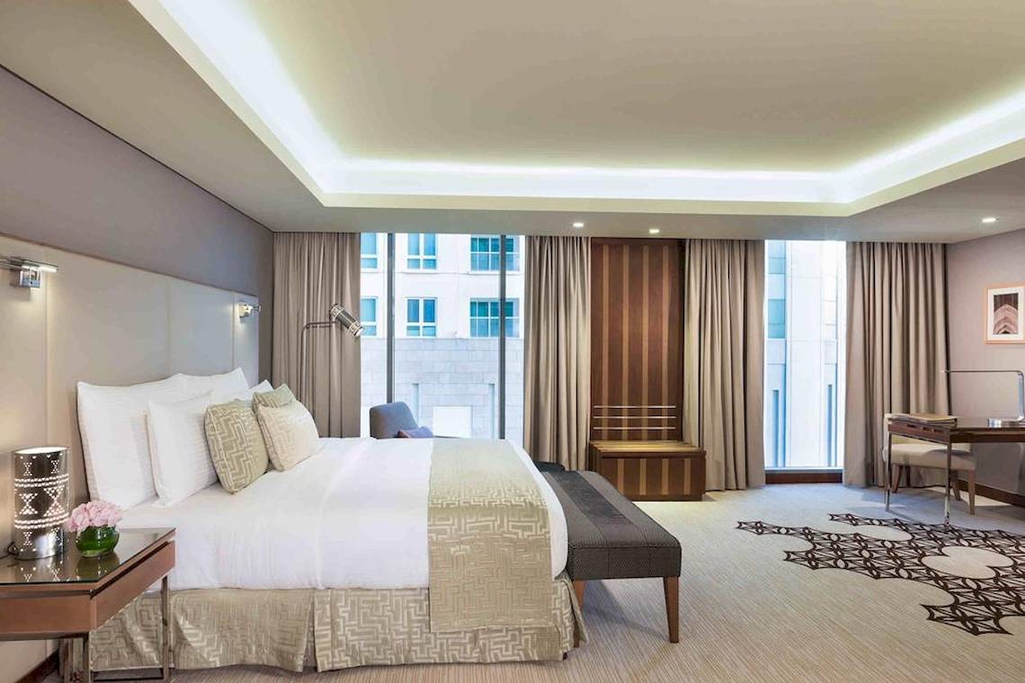 Hotelzimmer im Grand Millennium Muscat mit großem Bett, Schreibtisch und Fenstern.
