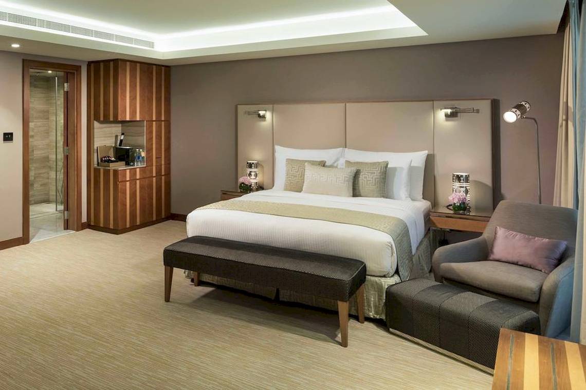 Innenansicht einer Hotelsuite im Grand Millennium Muscat mit großem Bett, Sitzbereich und moderner Einrichtung.