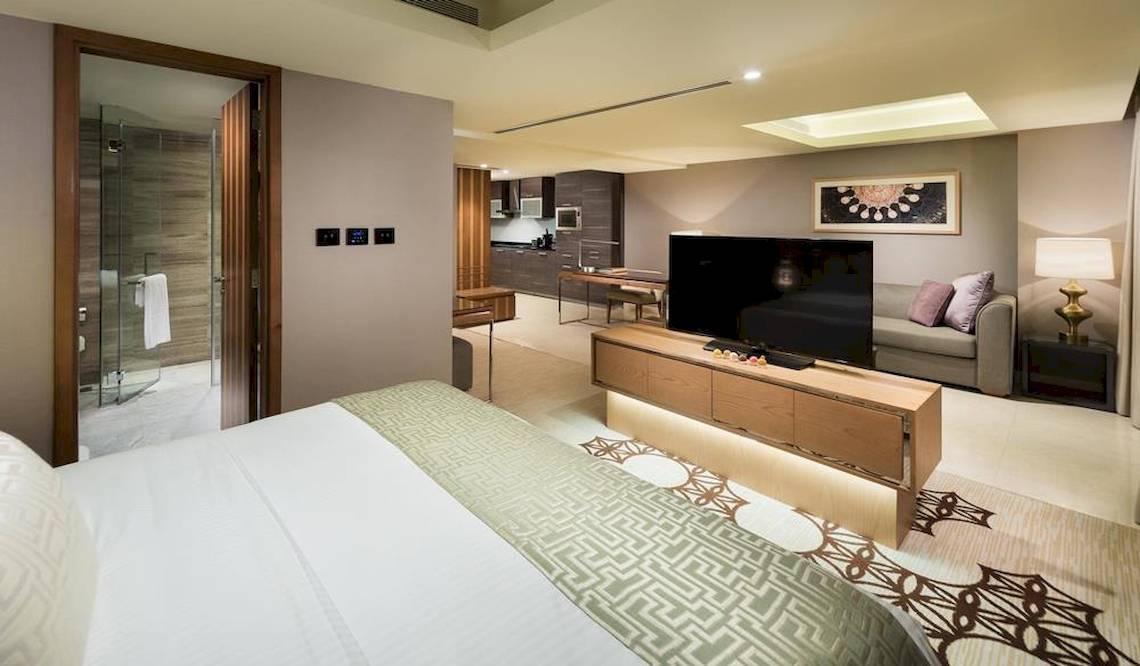 Innenansicht einer Suite im Grand Millennium Muscat mit Bett, Fernseher, Sofa und Dusche