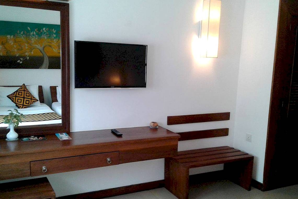 Innenansicht eines Hotelzimmers mit Fernseher, Spiegel, Nachttisch und Bank.
