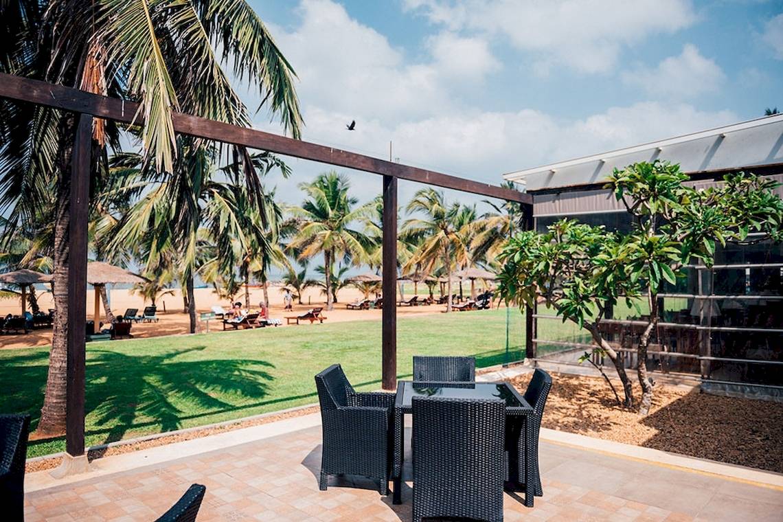 Außenbereich des Goldi Sands Hotels mit Tisch, Stühlen und Blick auf Palmen und Meer