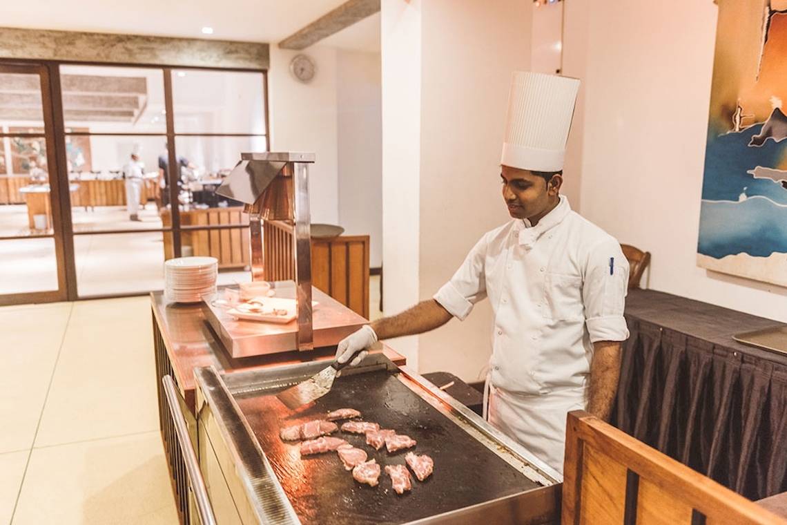 Koch in einem weißen Kochmütze, der Fleisch auf einem Grill in einem Hotel kocht.