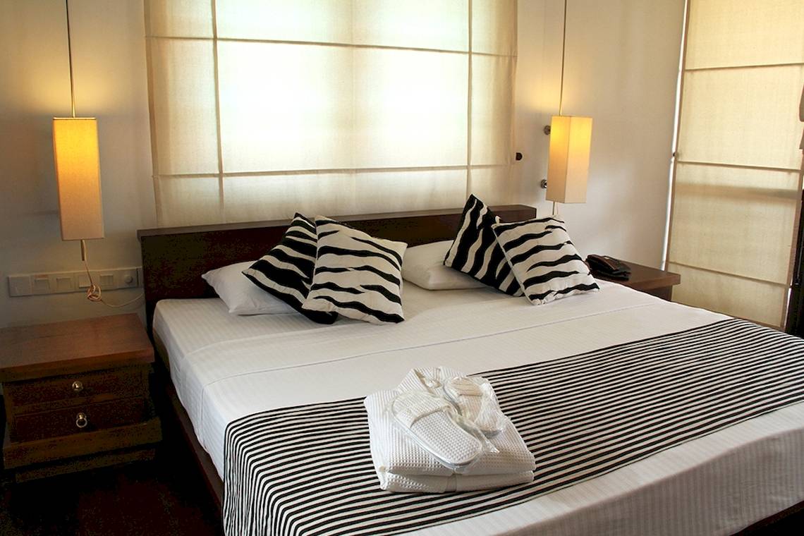 Doppelbett im Schlafzimmer des Goldi Sands Hotels mit weißen Laken und schwarzen und weißen Kissen.