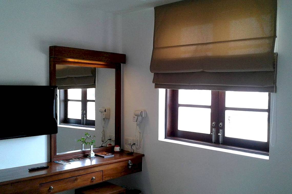 Zimmer im Goldi Sands Hotel mit Fernseher, Spiegel und Fenster mit Rollos.