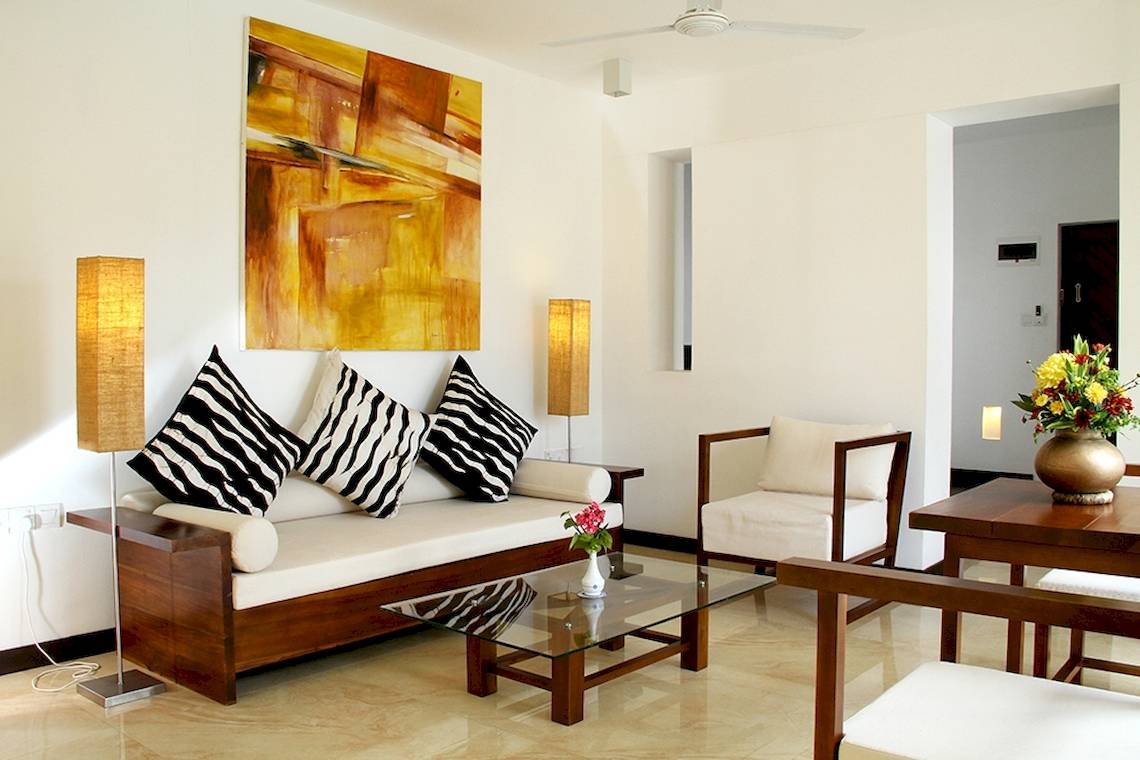Wohnzimmer im Goldi Sands Hotel mit weißer Couch, schwarzen und weißen Kissen, Glastisch und Lampe.