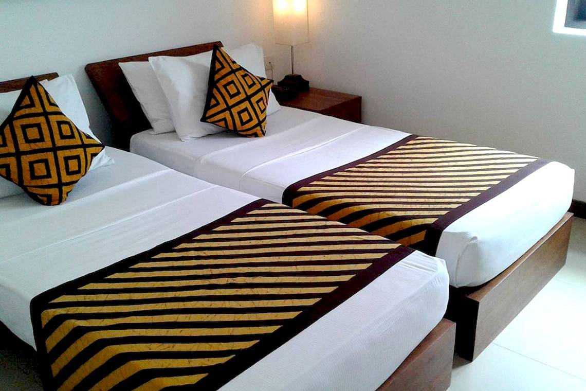 Zwei Betten im Goldi Sands Hotel mit farbigen Kissen und gestreiften Decken.