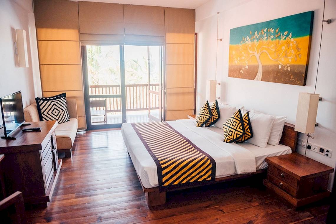 Hotelzimmer von Goldi Sands mit großem Bett, Sofa und Balkon.