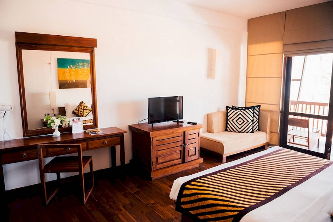 Ein elegantes Hotelzimmer von Goldi Sands mit einem großen Bett, einem Schreibtisch und einem Fernseher.