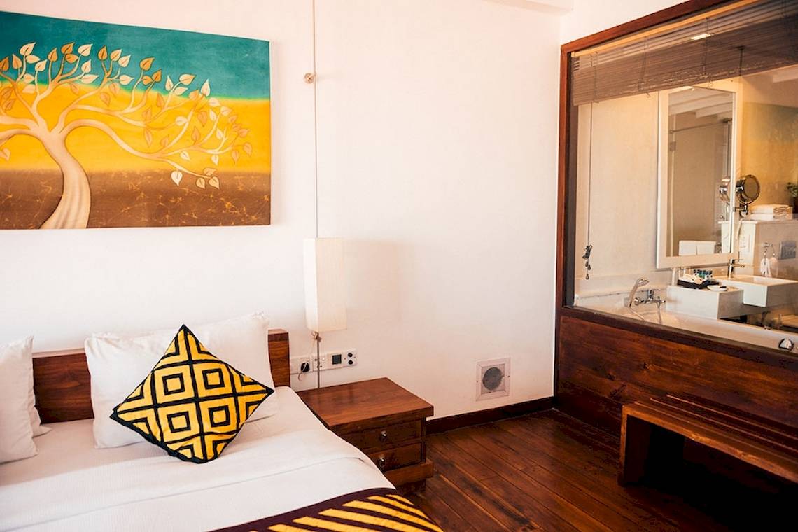 Hotelzimmer im Goldi Sands mit Bett, Kissen, Nachttisch und Badspiegel.