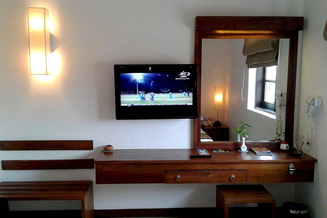 Ein Hotelzimmer mit Fernseher an der Wand, Spiegel und Schreibtisch davor.