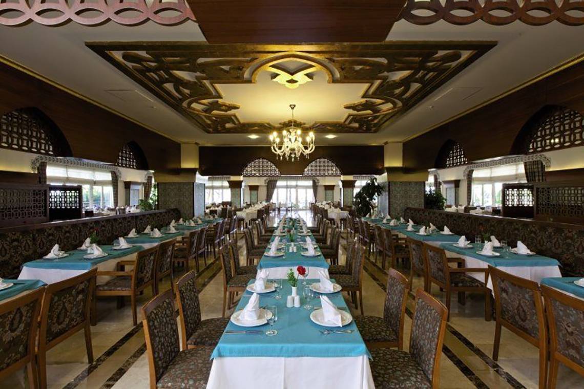 Restaurant im Adalya Bliss Hotel mit gedeckten Tischen und einer langen Tafel in der Mitte.