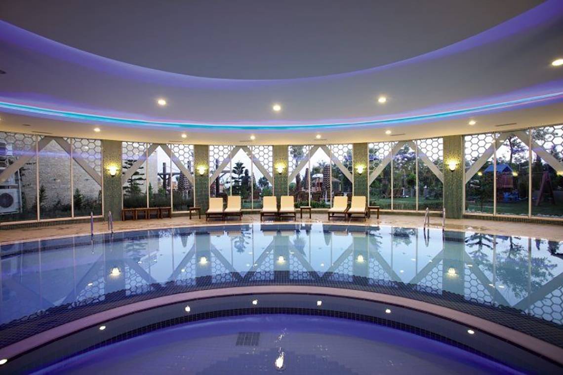 Innenpool im Adalya Bliss Hotel mit Lounge-Liegen und blauer Beleuchtung.