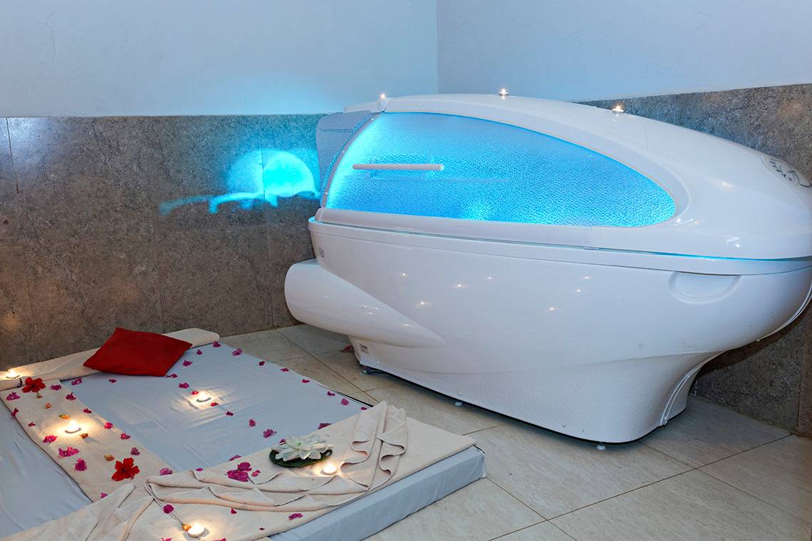 Ein Zimmer im Three Corners Rihana Inn Resort mit einer weißen Cryosauna und einem Bett, das mit roten Rosenblättern und Kerzen dekoriert ist.
