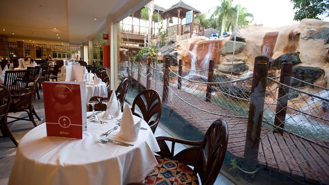 Restaurantbereich des Maspalomas Princess Hotels mit Tisch, Blick auf Wasserfall und Gehweg