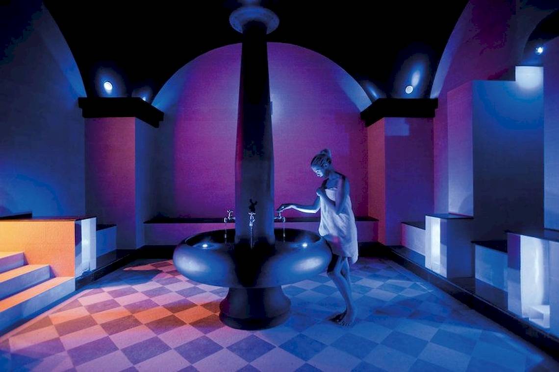 Eine Frau steht in der Elite Suites by Rhodes Bay Sauna und wäscht ihre Hände an einem Brunnen.