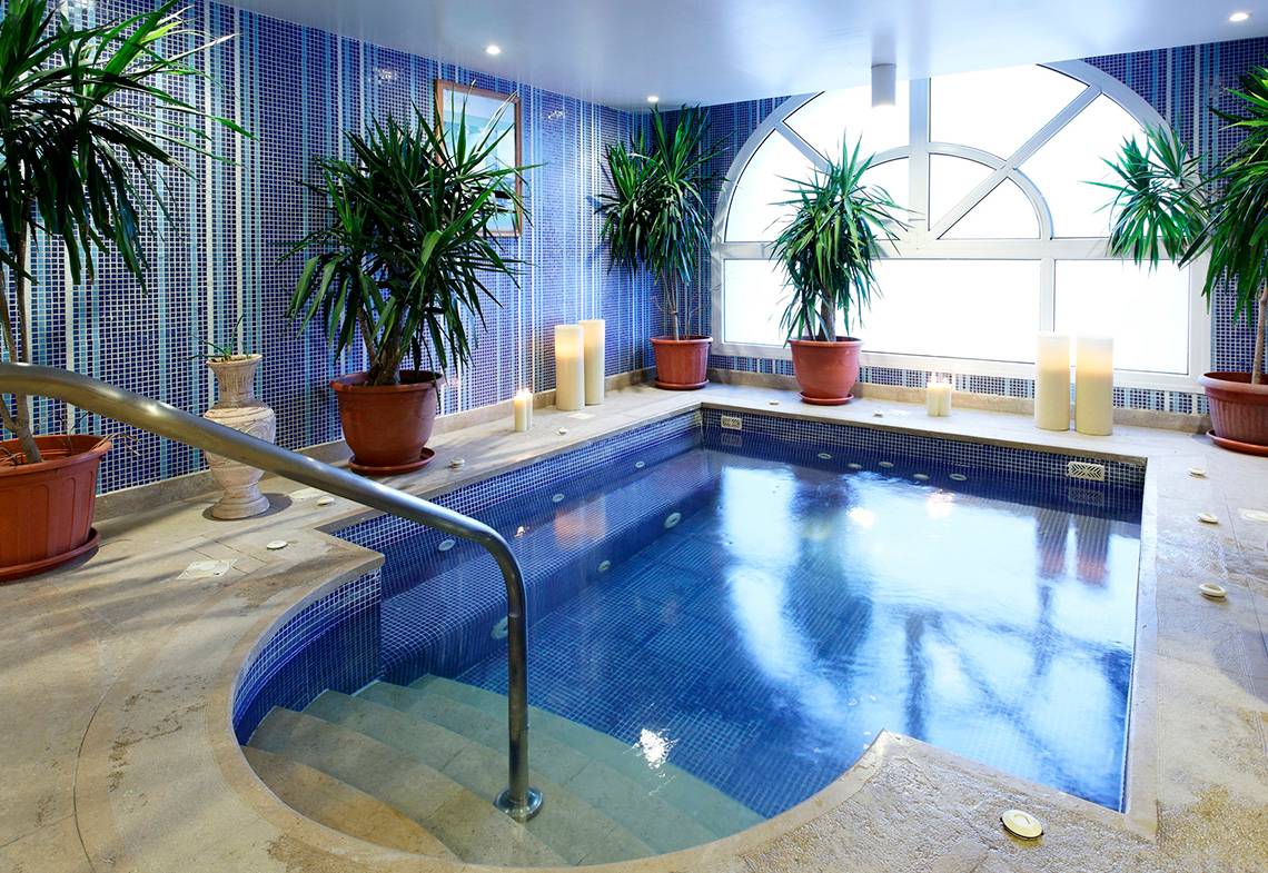 Ein kleiner, blau gefliester Poolraum im Drei Ecken Ocean View Hotel mit Pflanzen und Kerzen.