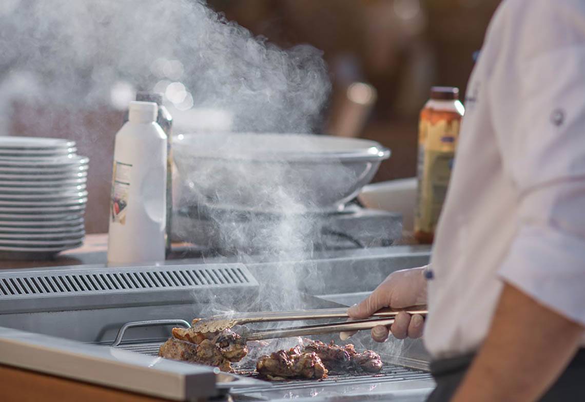 Ein Grillmeister brät Fleisch auf einem Grill im Cretan Dream Resort & Spa.