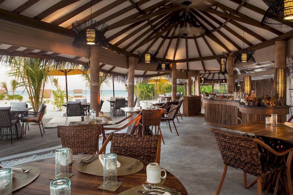 Innenansicht des Restaurants im Drift Thelu Veliga Retreat Hotel mit Tischen, Stühlen und Blick auf das Meer.