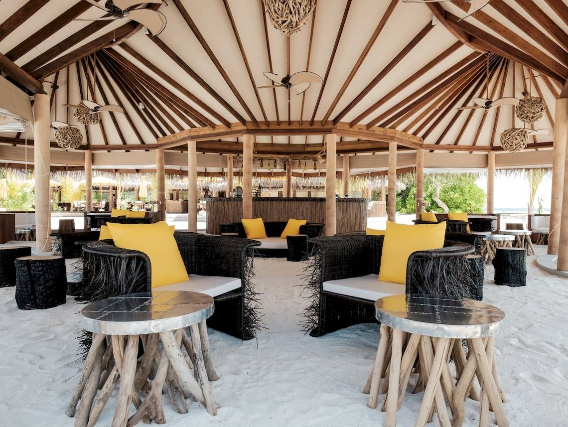 Strandlounge im Drift Thelu Veliga Retreat mit runden Sofas und Tischen auf weißem Sand.