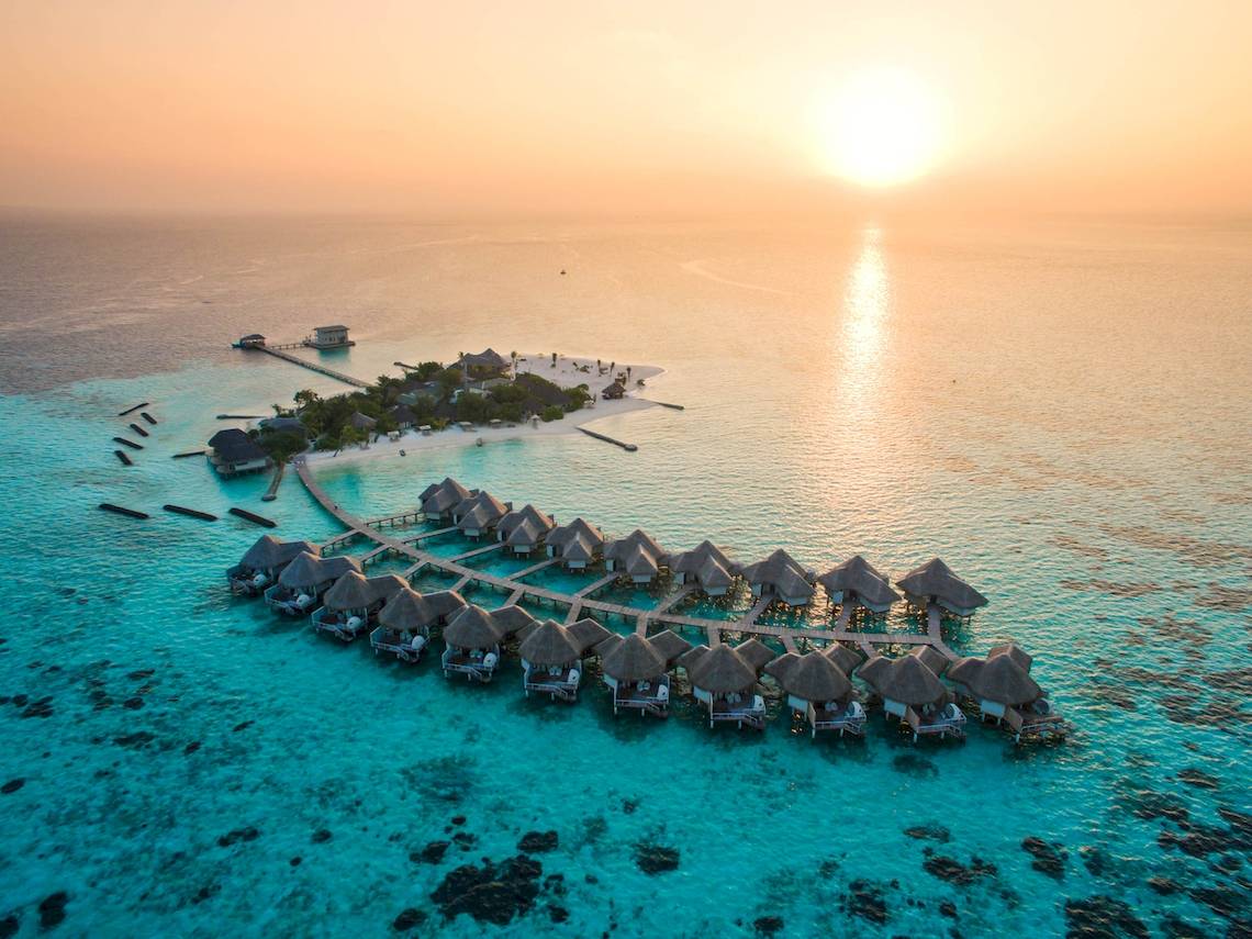 Luftaufnahme des Drift Thelu Veliga Retreats mit Wasserbungalows und Steg am Sonnenuntergang