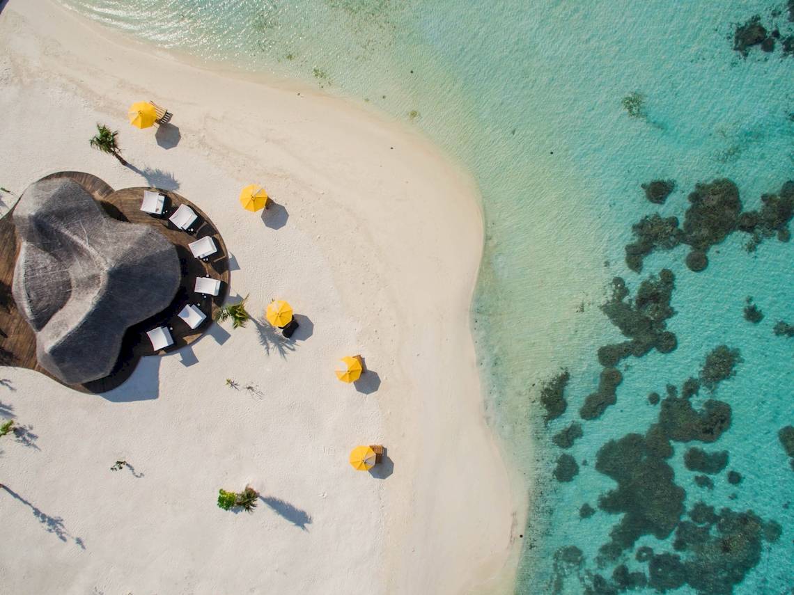 Luftaufnahme des Drift Thelu Veliga Retreat mit Strand, gelben Sonnenschirmen und Gebäuden